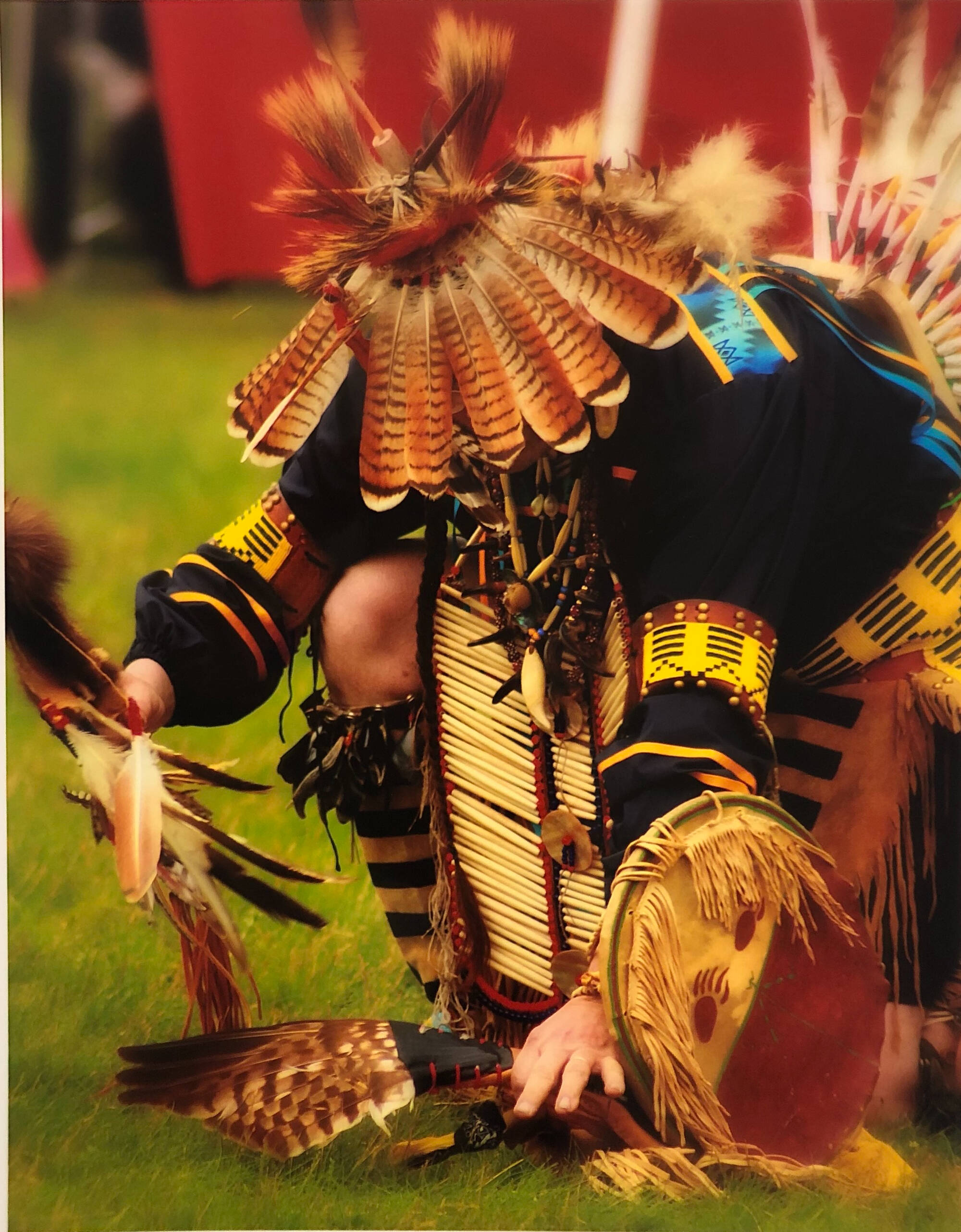 Color photograph of an indigenous person kneeling on the ground.